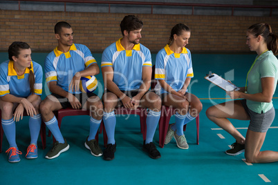 Coach discussing with volleyball players sitting on chairs