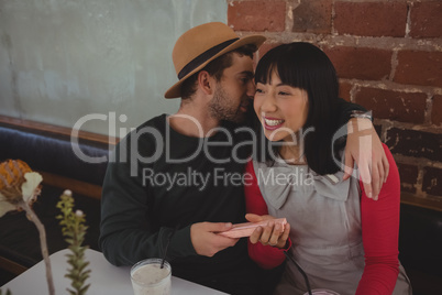 Man whispering in woman ear at cafe