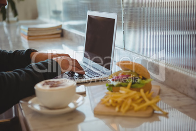 Cropped hands of man using laptop by coffee cup and French fries