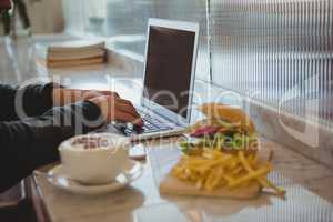 Cropped hands of man using laptop by coffee cup and French fries