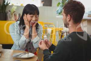 Man gifting ring to shocked woman in cafe