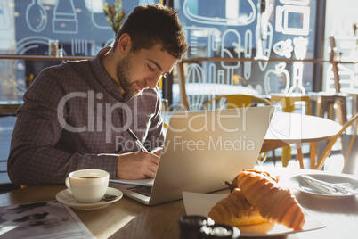 Businessman with laptop writing on paper in cafe