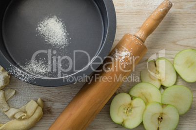 Overhead view of rolling pin by apple slices and container
