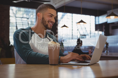 Man with milkshake glass using laptop in cafe