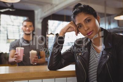 Portrait of woman with friend holding milkshake glasses in cafe