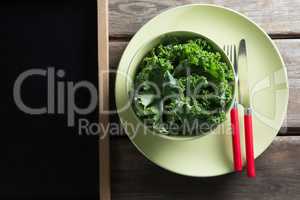 Overhead view of kale in bowl on plate by blackboard over table
