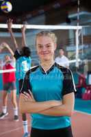 Smiling female volleyball player standing with arms crossed in the court