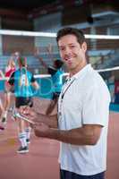 Smiling coach writing on clipboard in the volleyball court