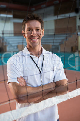 Smiling coach standing behind the net with arms crossed in volleyball court