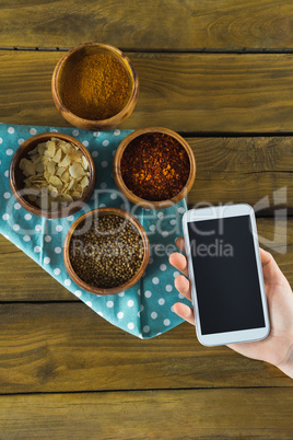 Hand holding mobilephone and various spices in bowl