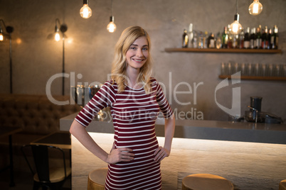 Portrait of beautiful woman standing with hands on hip at counter