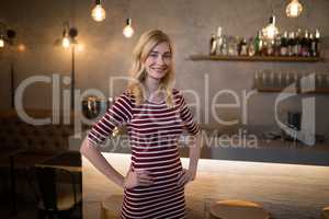 Portrait of beautiful woman standing with hands on hip at counter