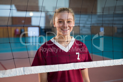 Smiling female volleyball player standing behind the net