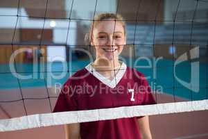 Smiling female volleyball player standing behind the net