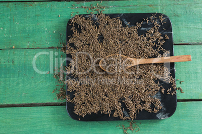 Cumin with spoon in tray on wooden table