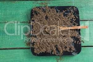 Cumin with spoon in tray on wooden table