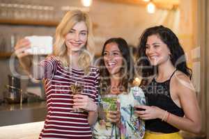 Portrait of female friends taking selfie while having drinks