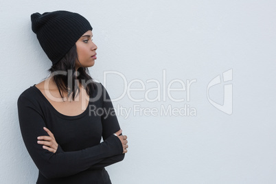 Thoughtful woman with arms crossed against white wall