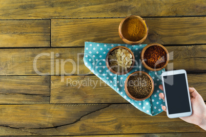 Hand holding mobilephone and various spices in bowl