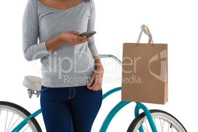 Woman using mobile phone while standing by bicycle