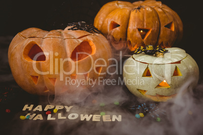 Happy Halloween text with jack o lanterns by candies and decorations