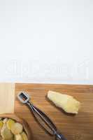 Directly above view of peeler and fresh ginger on wooden cutting board