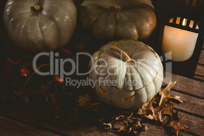White jack o lanterns with autumn leaves by candle on table