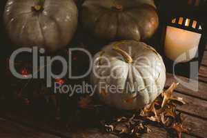 White jack o lanterns with autumn leaves by candle on table