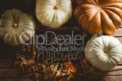 Happy Halloween text on slate by pumpkins amidst autumn leaves