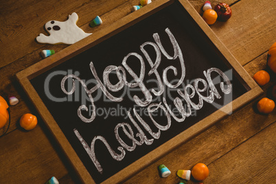 Slate with happy Halloween text by candies on wooden table