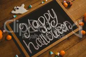 Slate with happy Halloween text by candies on wooden table