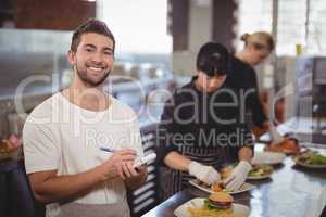 Smiling waiter standing against female chefs preparing food in kitchen