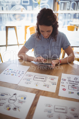 Young woman using digital table while sitting at table with chart papers