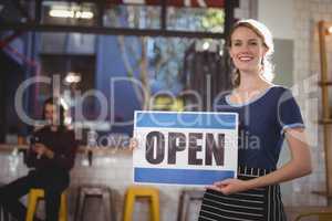 Portrait of smiling young waitress holding open sign placard