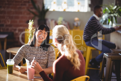 Cheerful female friends talking while sitting with fresh drinks at table