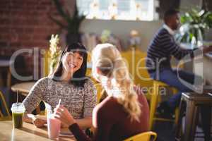 Cheerful female friends talking while sitting with fresh drinks at table