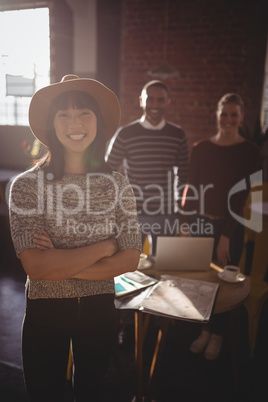 Portrait of smiling woman standing with arms crossed against colleagues