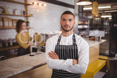 Portrait of confident waiter standing with arms crossed at  coffee shop