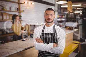 Portrait of confident waiter standing with arms crossed at  coffee shop