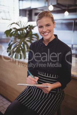 Portait of smiling young waitress sitting with clipboard at coffee shop