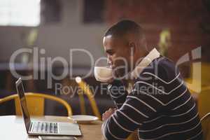 Side view of young man drinking coffee while looking at laptop