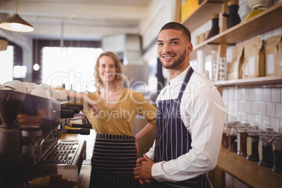 Portrait of smiling young waiter and waitress standing by espresso maker