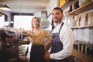 Portrait of smiling young waiter and waitress standing by espresso maker