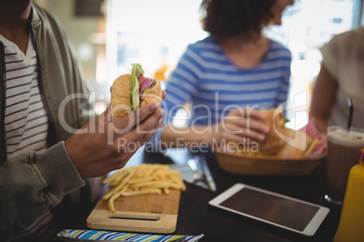 Midsection man holding fresh hamburger while sitting in cafe