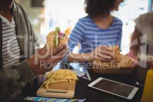 Midsection man holding fresh hamburger while sitting in cafe