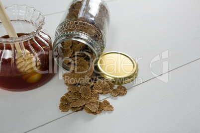 Jar of honey and wheat flakes spilling out of bottle