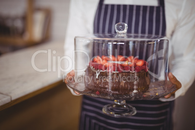 Midsection of waiter holding fresh cake on glass cakestand