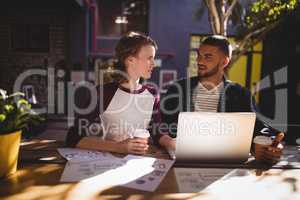 Young creative professionals talking while sitting with laptop at coffee shop