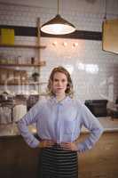 Portrait of confident young pretty waitress standing with hands on hip