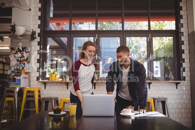 Man gesturing at laptop while standing by woman